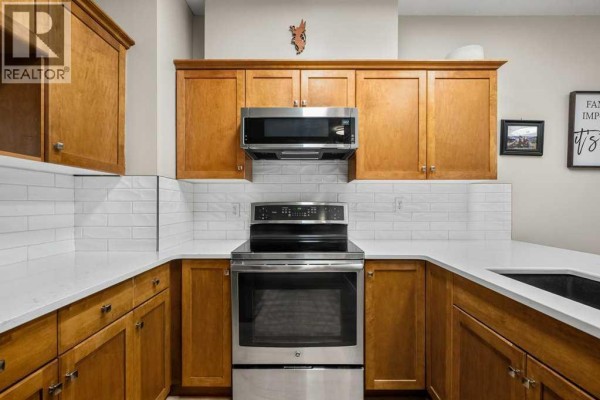Kitchen sink and island with view into a living area with a sliding glass door and patio. - 1204, 720 Willowbrook Road Nw, Airdrie