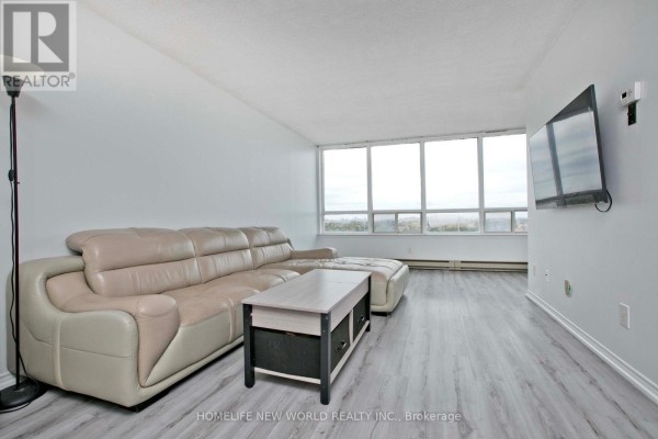 Living room with a sectional sofa, coffee table, television, and large windows with a view. - 1204 - 160 Alton Towers Circle, Toronto