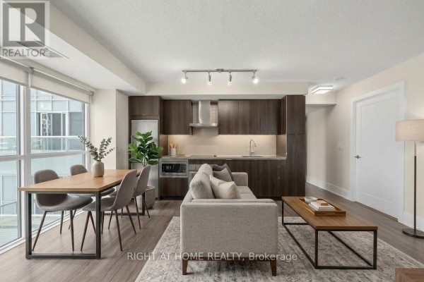 Open concept living and dining area with a kitchen, sofa, dining table, and city view. - 1204 - 300 Front Street W, Toronto