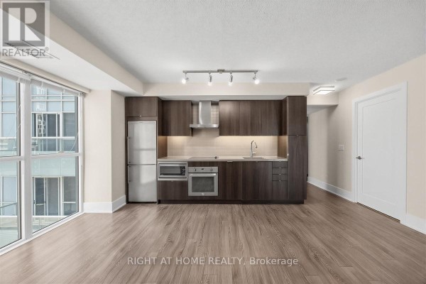 Open concept living and kitchen area with dark wood cabinets, stainless steel appliances, and city view. - 1204 - 300 Front Street W, Toronto