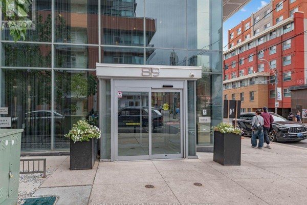 Entrance to a modern apartment building with glass doors and planters. - 1204 - 89 Mcgill Street, Toronto