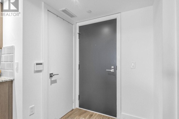 Interior view of a hallway with white walls and a dark grey front door. - 1204 - 89 Mcgill Street, Toronto