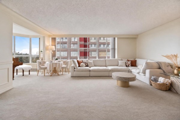 Spacious living and dining area with large windows overlooking buildings and trees, featuring a sectional sofa. - 1204 11920 80 Avenue, Delta