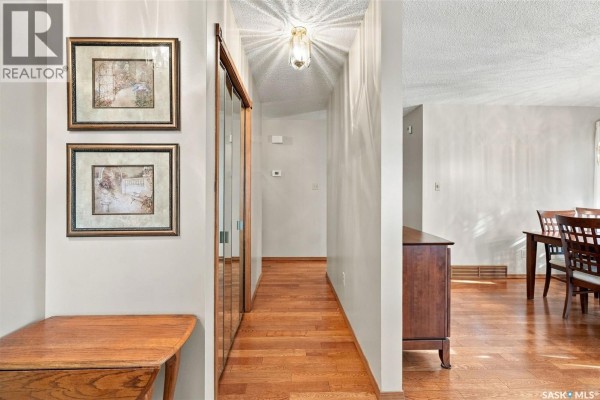 Interior hallway with hardwood floors, a mirrored closet door, and framed art on the wall. - 1204 Lapchuk Crescent N, Regina