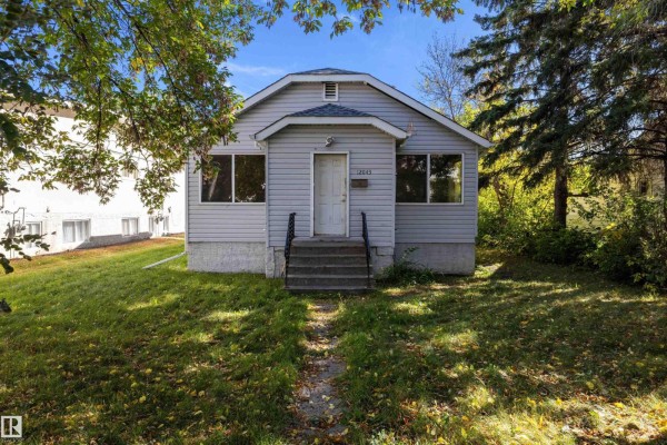 View of a light gray bungalow with a front walkway and lawn, framed by trees. - 12043 87 St Nw, Edmonton