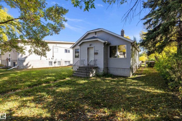 Side view of the light gray bungalow, showing the lawn and surrounding trees. - 12043 87 St Nw, Edmonton