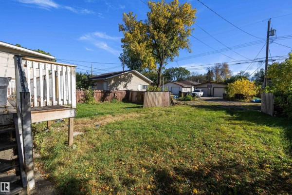 Backyard view with a wooden deck, grass, trees, and garages in the distance. - 12043 87 St Nw, Edmonton