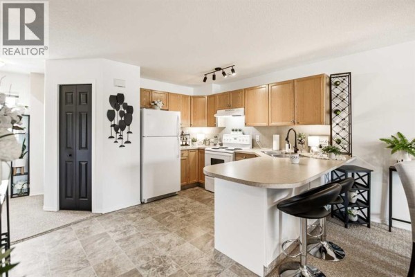 Kitchen with light wood cabinets, white appliances, a curved breakfast bar, and beige floor tiles. - 1205, 5220 50a Avenue, Sylvan Lake