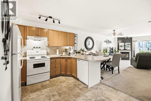 View of kitchen, breakfast bar, dining area with round table, and living room with fireplace. - 1205, 5220 50a Avenue, Sylvan Lake