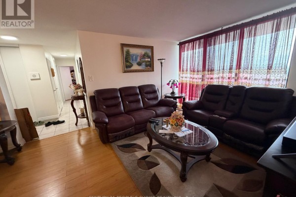 Living room with hardwood floors, two brown sofas, coffee table, rug, and doorway to hallway. - 1205 - 17 Knightsbridge Road, Brampton