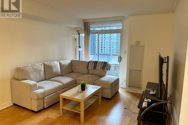 Living room with light beige sectional sofa, light wood coffee table, and television. - 1205 - 3880 Duke Of York Boulevard, Mississauga
