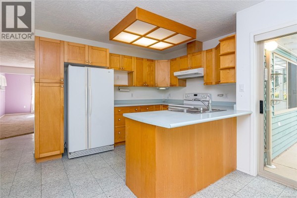 Kitchen with light wood cabinets, a white refrigerator, and a central island with a light-colored countertop. - 1205 Corcan Rd, Qualicum Beach