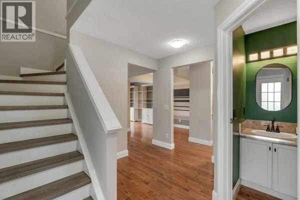 Hallway with hardwood floors, a staircase, and doorways leading to other rooms. - 1205 Signal Hill Green Sw, Calgary