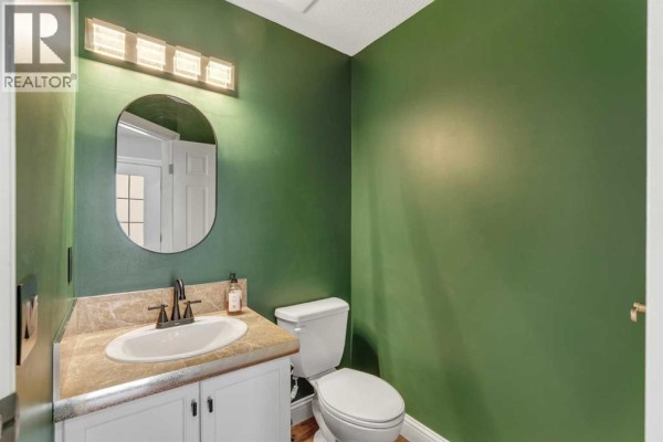 Powder room with green walls, a vanity, toilet, and a rounded mirror. - 1205 Signal Hill Green Sw, Calgary