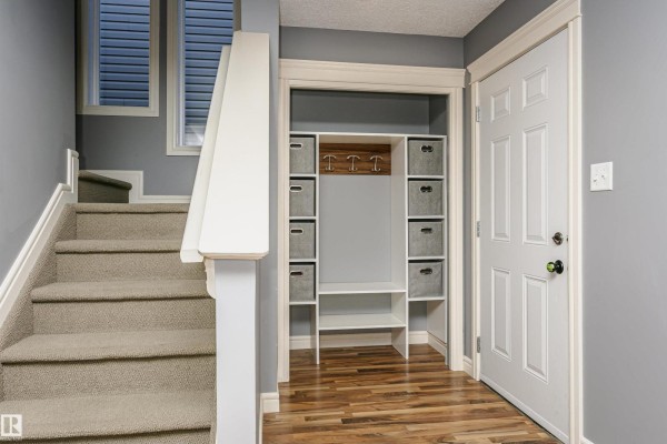 Interior foyer with carpeted stairs, built-in storage unit, and wood-look flooring. - 12051 18 Av Sw Sw, Edmonton