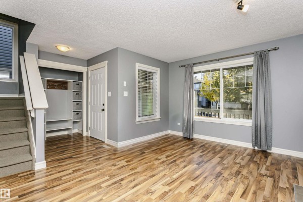 Living room with grey walls, large window, wood flooring, and access to foyer. - 12051 18 Av Sw Sw, Edmonton