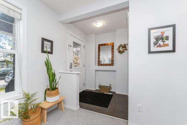Interior entryway with light gray walls, tile floor, and a wooden bench with plants. - 12059 19 Av Sw, Edmonton