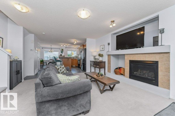 Living room with a gray sofa, coffee table, gas fireplace with tile surround, and a mounted TV. - 12059 19 Av Sw, Edmonton
