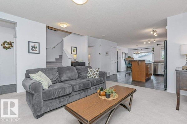 Living room with a gray sofa, coffee table, and view into the kitchen with a breakfast bar. - 12059 19 Av Sw, Edmonton