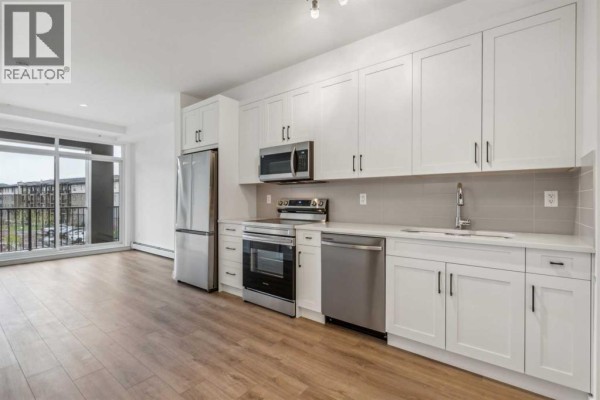 A modern kitchen with white cabinets, stainless steel appliances, and light wood flooring. - 1206, 14910 1 Street Nw, Calgary