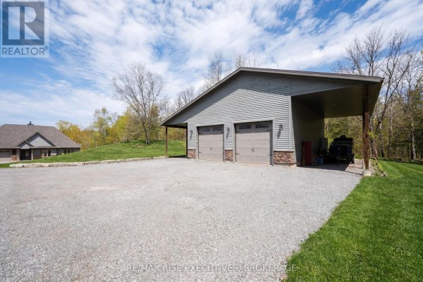 Two-car garage with a detached covered carport, situated on a gravel driveway. - 1206b Burnt Hills Road, Frontenac