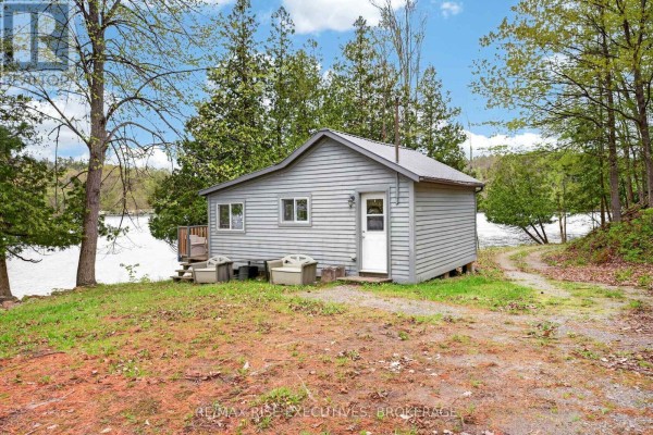 Spacious living room with a stone fireplace, vaulted ceilings, large windows, and open access to the kitchen and dining area. - 1206b Burnt Hills Road, Frontenac