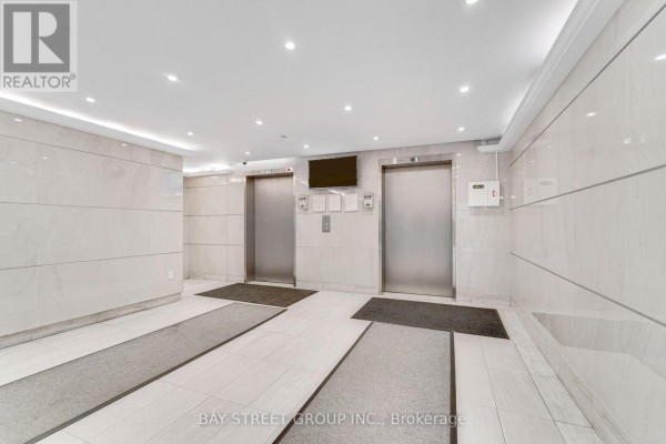 Two silver elevator doors in a well-lit lobby with marble-like wall tiles. - 1207 - 10 Stonehill Court, Toronto