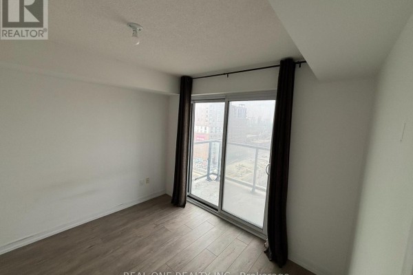 Empty room with light wood-look flooring, white walls, and a sliding glass door to a balcony. - 1207 - 1420 Dupont Street, Toronto