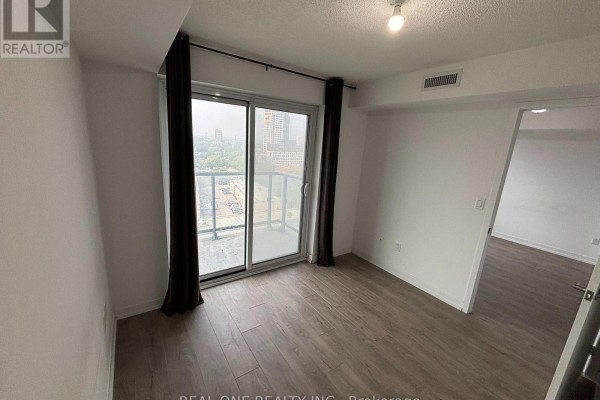 Empty room with light wood-look flooring, white walls, and sliding glass doors to a balcony and an open doorway. - 1207 - 1420 Dupont Street, Toronto