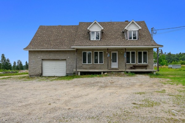 Front exterior of a two-story house with a garage, dormer windows, and light-colored brick. - 1207z Route Principale, Aumond