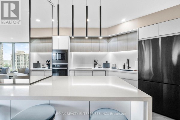 A contemporary kitchen with a waterfall island and sleek white cabinetry. - 1208 - 1 Palace Pier Court, Toronto