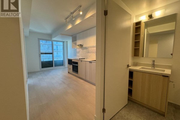 View from hallway into an open-concept living area with a kitchen and balcony access. - 1208 - 252 Church Street, Toronto