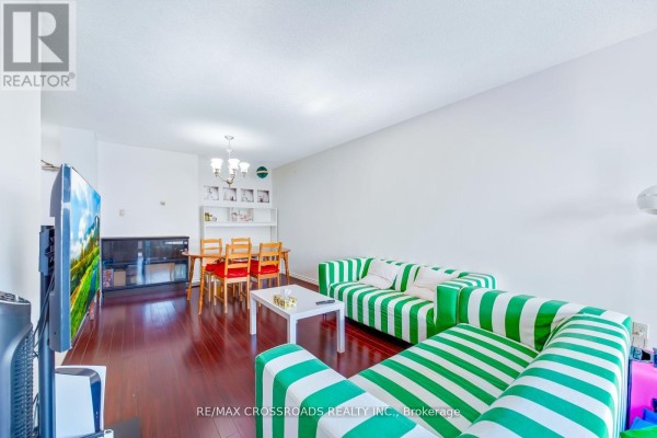 Living and dining area with a striped sofa, wooden dining table, and dark wood floors. - 1208 - 340 Dixon Road, Toronto