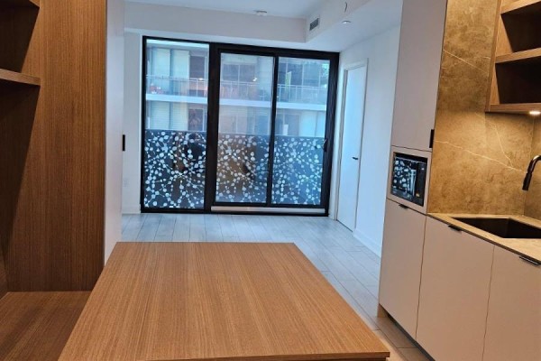 View from inside the apartment looking towards the balcony doors and the kitchen area. - 1208 - 55 Charles Street E, Toronto