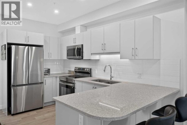 Close-up of a modern kitchen with white subway tile backsplash, granite countertops, stainless steel appliances, and a double sink. - 1209, 81 Arbour Lake View Nw, Calgary
