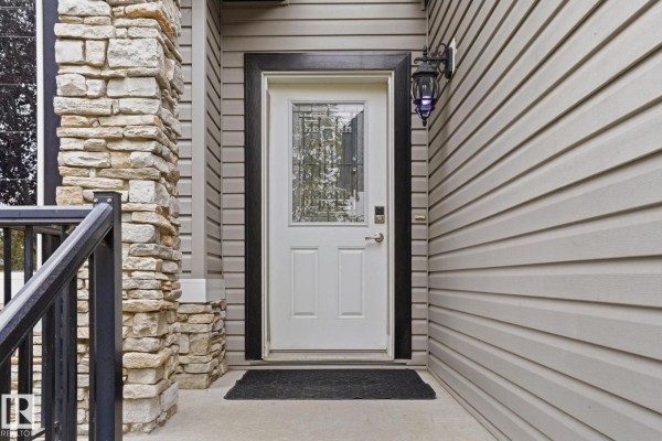 Close-up of the front entrance door with a glass pane and black trim, surrounded by stone and siding. - 1209 Cunningham Dr Sw Sw, Edmonton