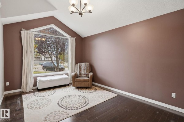 Living room with dark hardwood floors, brown walls, a large arched window, and a single armchair. - 1209 Cunningham Dr Sw Sw, Edmonton