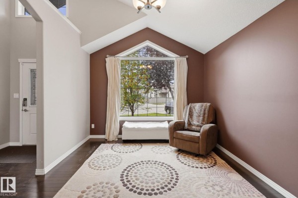 Room with a vaulted ceiling, dark hardwood floors, brown walls, a large window with white curtains, and a patterned rug. - 1209 Cunningham Dr Sw Sw, Edmonton