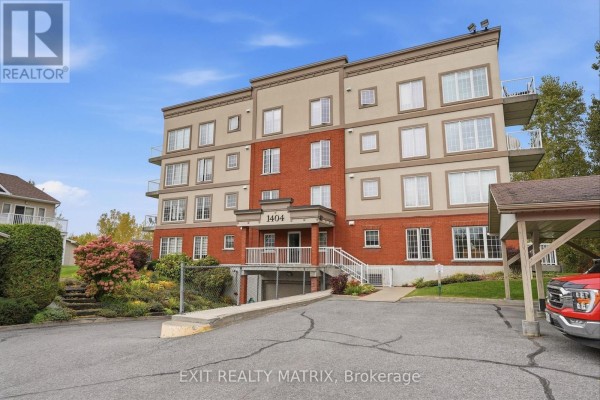 View of the apartment building entrance with a paved driveway and parking spaces. - 121 - 1404 Clement Street, Hawkesbury