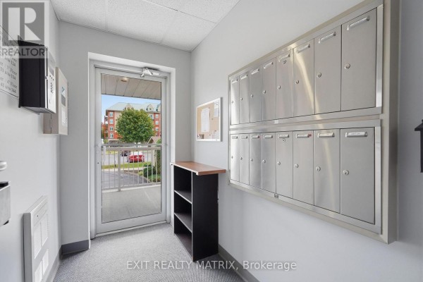 Interior hallway with a glass door, mailboxes, and a small dark wood shelf unit. - 121 - 1404 Clement Street, Hawkesbury