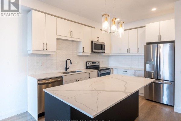 Kitchen view showing white cabinets, island with quartz countertop, and stainless steel appliances. - 121 - 3900 Savoy Street, London South