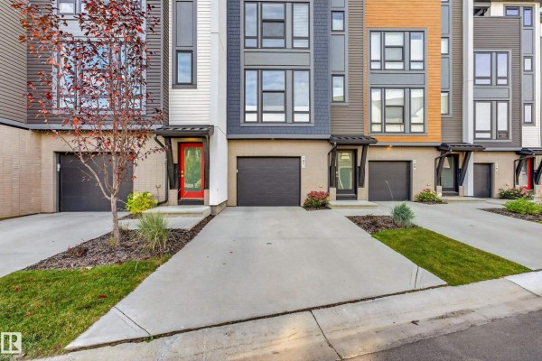 Close-up front view of townhouse entrances and garages with concrete driveways and landscaping. - #121 1304 Rutherford Rd Sw, Edmonton