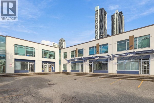 Exterior view of a commercial building with multiple units and parking spaces, tall buildings in background. - 121 3989 Henning Drive, Burnaby