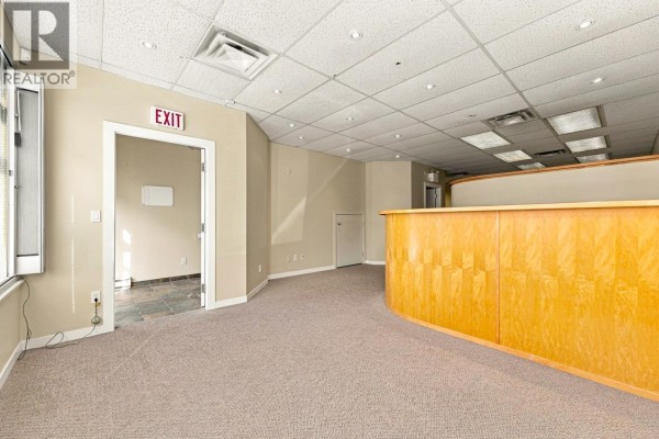 Interior office space with carpet, wood reception desk, and an exit sign above a doorway. - 121 3989 Henning Drive, Burnaby