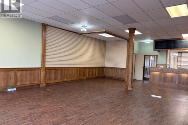 Wide view of an empty commercial interior with wood trim, slatted walls, and dark laminate flooring. - 121 Center Street W, Vulcan