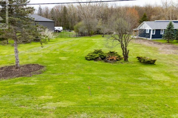 Expansive grassy lot with mature trees, bushes, and multiple buildings visible in the distance. - 121 Dodge Drive, Kitchener
