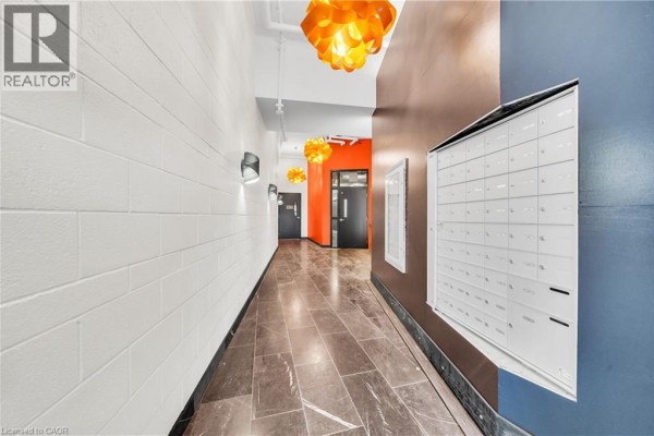 Hallway with white brick walls, dark grey tiled floor, and rows of white mailboxes. - 121 King Street E Unit# 605, Hamilton