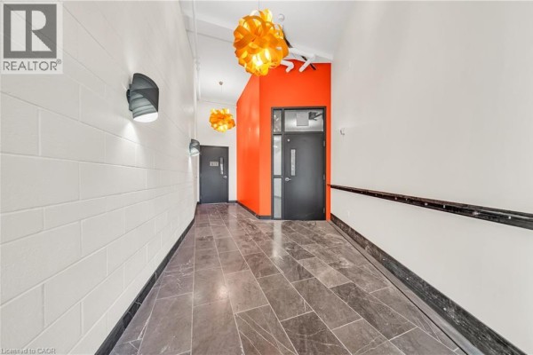 Hallway with orange accent wall, dark doors, and decorative orange pendant lights. - 121 King Street E Unit# 605, Hamilton