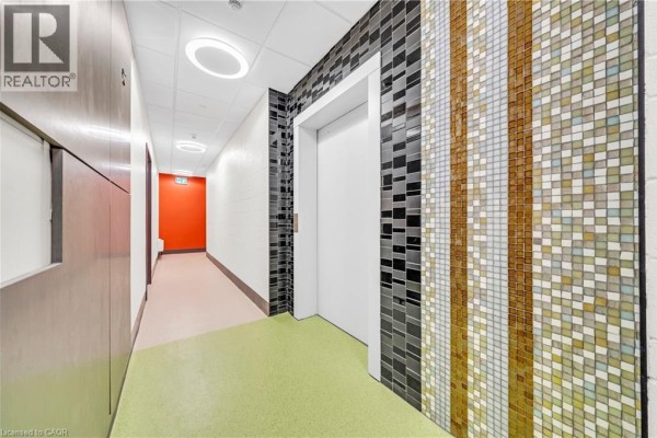 Hallway with a white elevator door and a colorful mosaic tile accent wall. - 121 King Street E Unit# 605, Hamilton