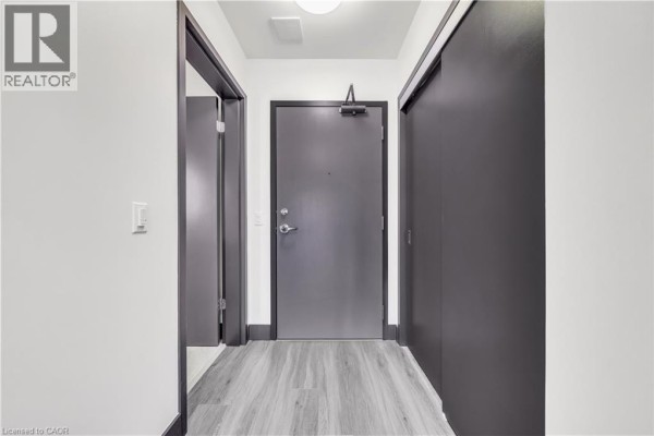 Interior hallway with a grey apartment door, white walls, and grey wood-look flooring. - 121 King Street E Unit# 605, Hamilton
